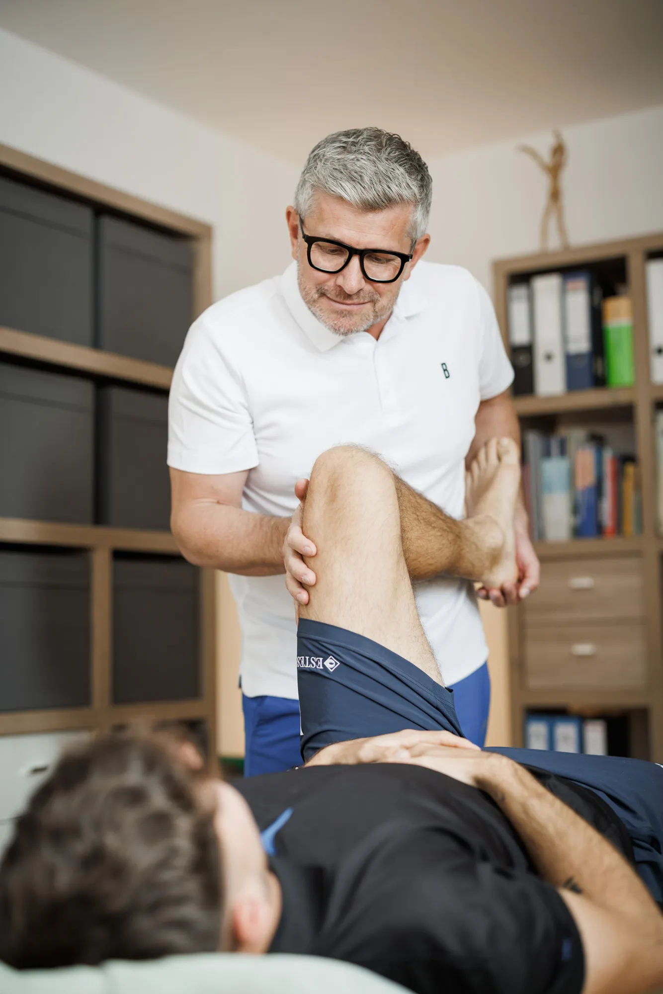 Physiotherapeut Rafal behandelt das Knie eines Patienten auf der Liege, Reportage-Portrait