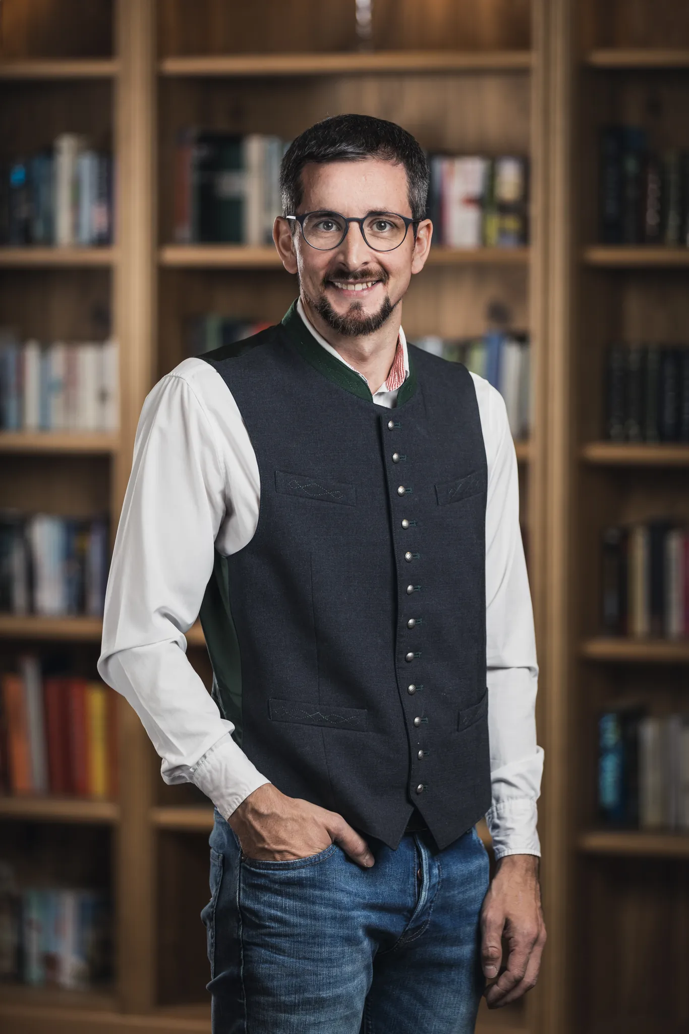 Mann mit Brille und Weste vor einem Bücherregal, Business Portrait