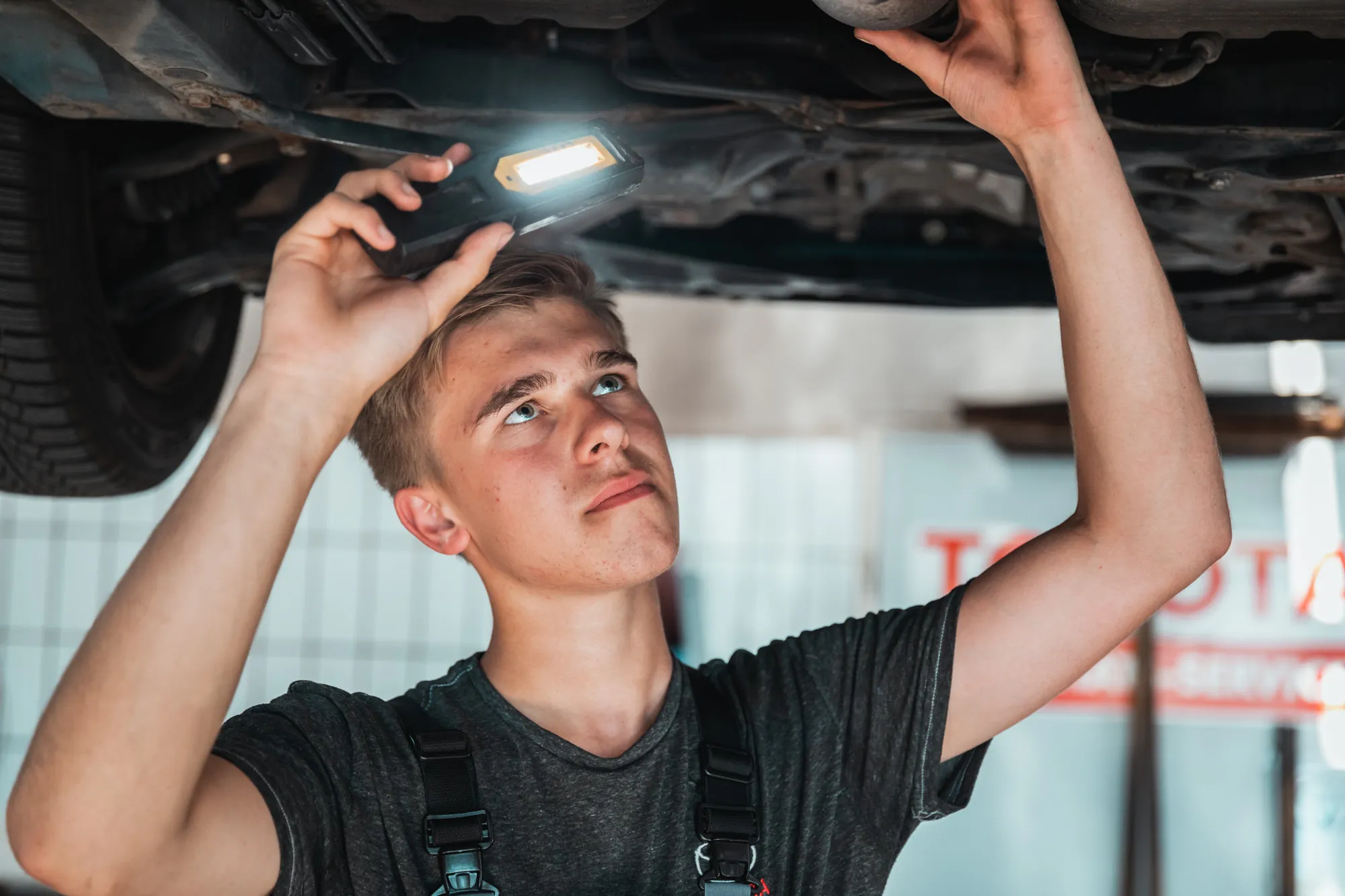 Lehrling arbeitet unter dem Fahrzeug auf der Hebebühne, Werkstattreportage