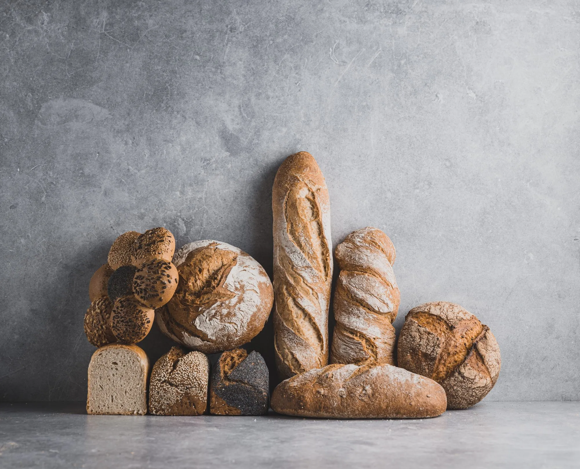Baguette, Brotlaibe und Kastenbrot vor grauem Betonhintergrund, Brotschmiede