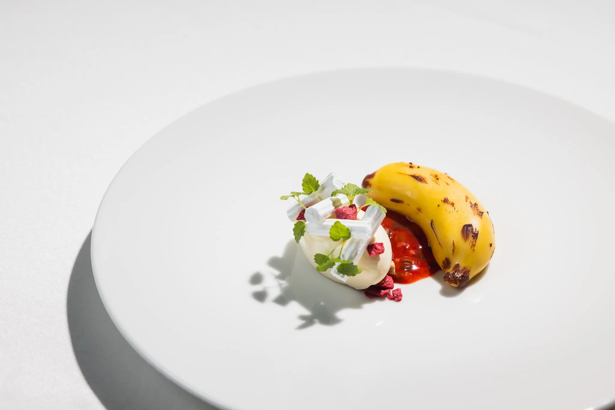 Dessert mit karamellisierter Banane, Beeren und Creme auf weißem Teller im Tageslicht