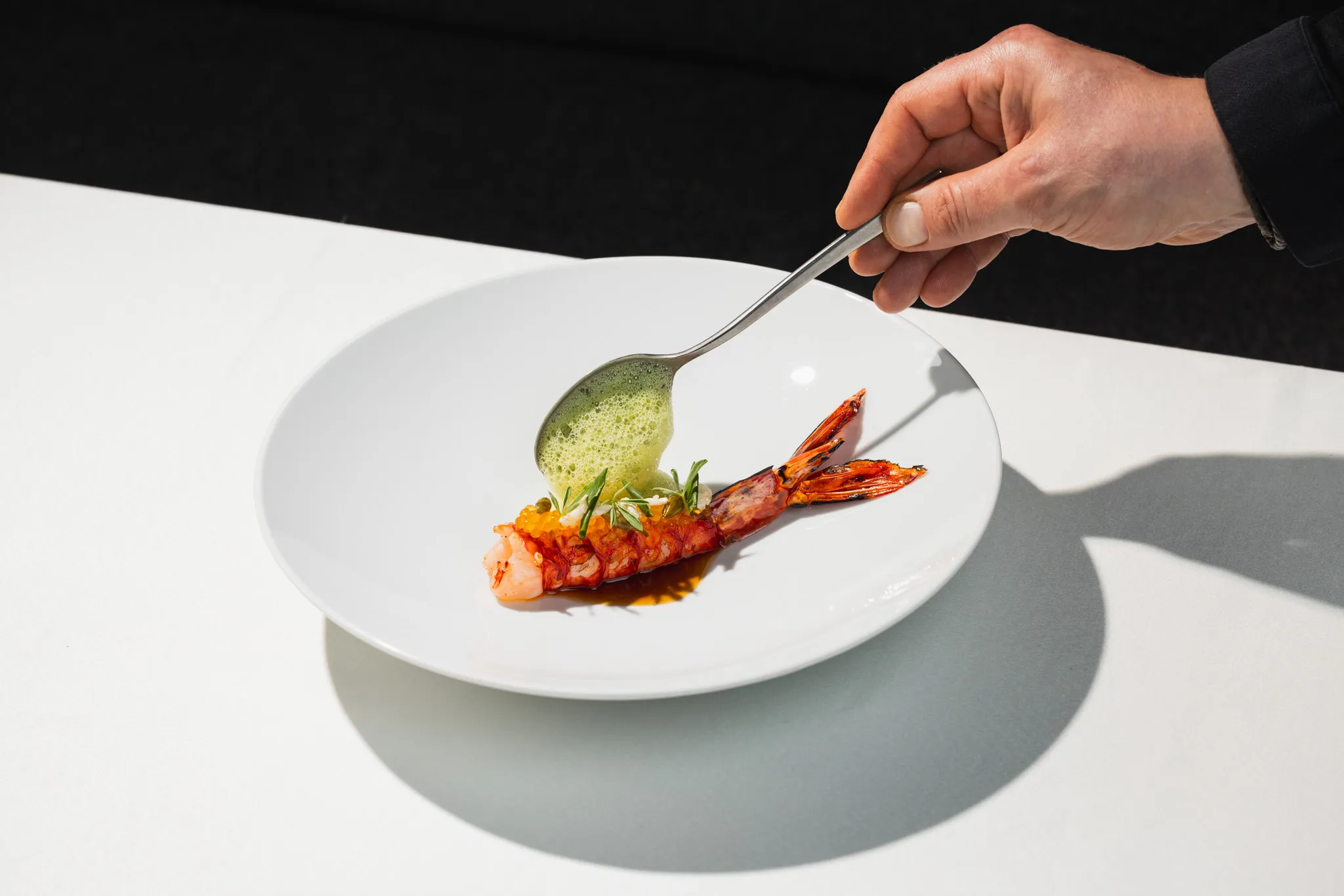 Kräutersauce wird mit dem Löffel neben eine rote Garnele auf den Teller gegeben