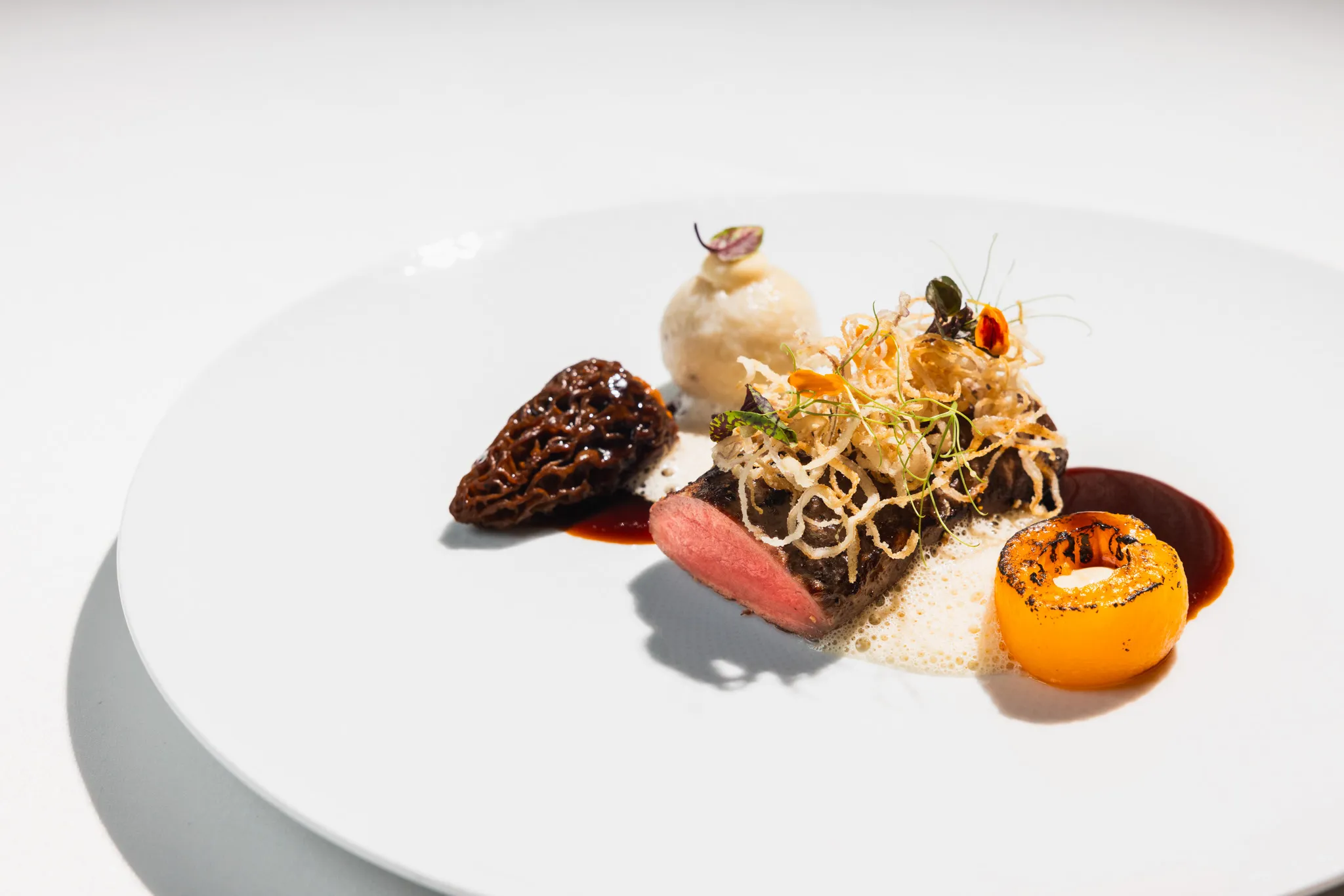 Hauptgang mit Morchel, rosa Fleisch, Kürbis und frittierten Kartoffelfäden auf weißem Teller