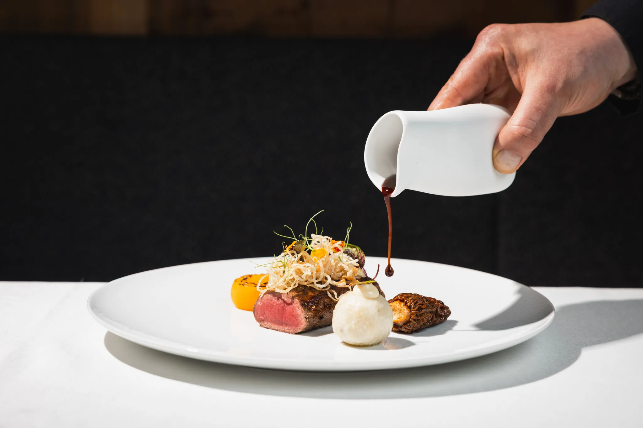 Sauce wird aus einem Kännchen über Fleisch, Morchel und Knödel gegossen, Küche in Aktion