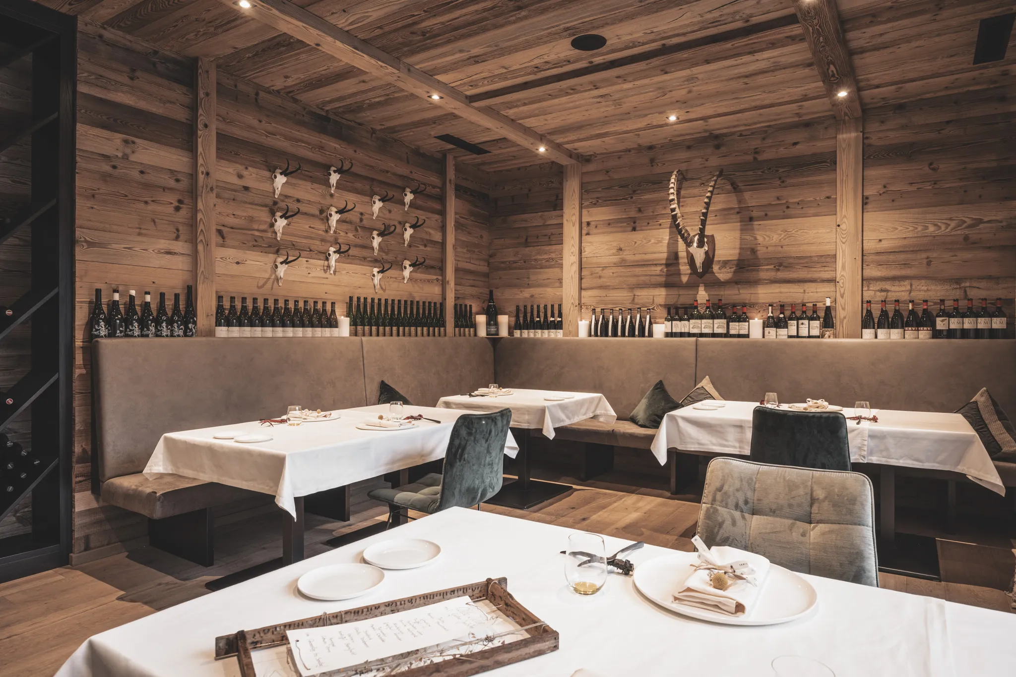Gedeckte Tische in der Stube aus Altholz mit Steinbockgehörn und Weinwand