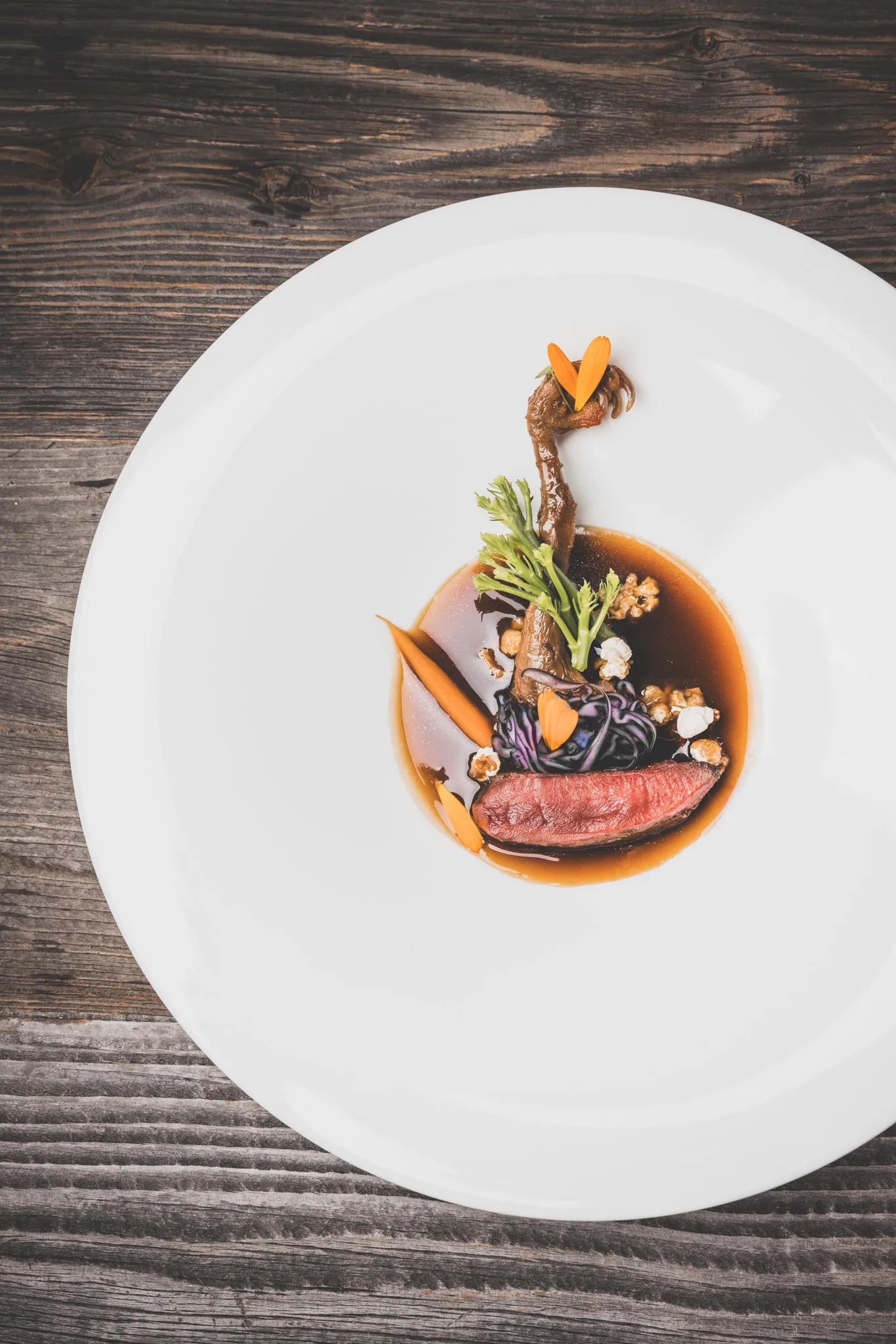 Wildgericht von oben auf weißem Teller, daneben dunkles Altholz, Foodfotografie