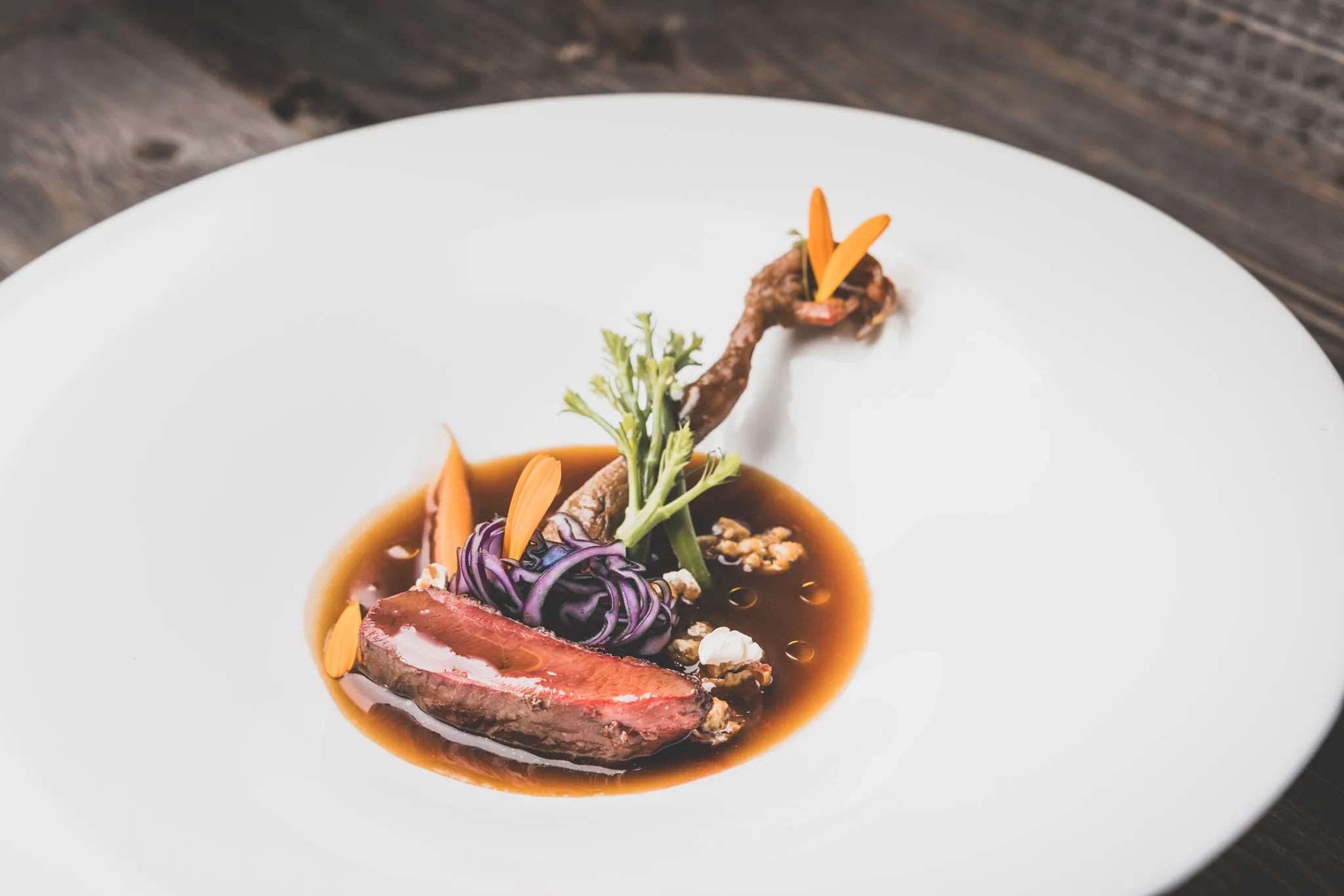 Rosa gebratenes Wild mit Jus, Rotkraut und Gemüse auf weißem Teller vor dunklem Altholz, Foodfotografie