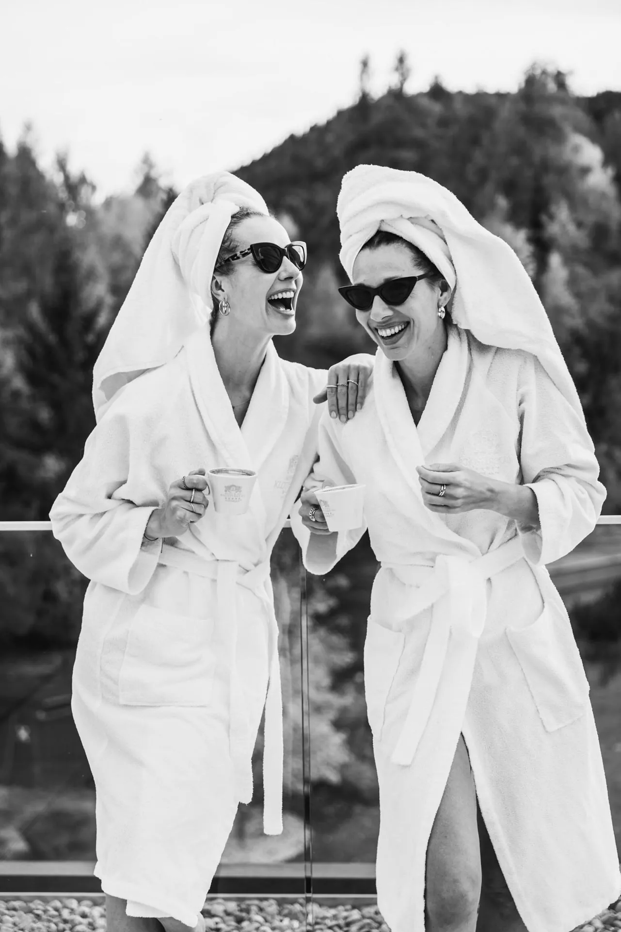 Zwei Freundinnen im Bademantel mit Sonnenbrillen lachen auf der Terrasse, Schwarz-Weiß, Hotel Klosterbräu